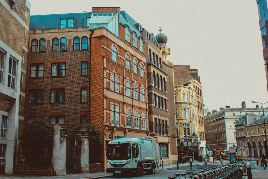 A busy commercial street viewed from a slightly elevated perspective, with a variety of small retail shops and cafes lining both sides of the pavement. The buildings are predominantly two to three sto